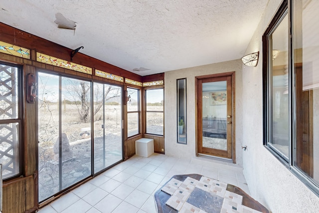 unfurnished sunroom with a textured ceiling, tile patterned floors, and a healthy amount of sunlight