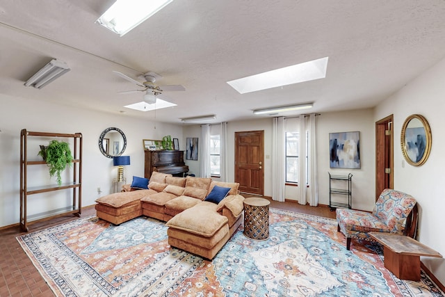 living room featuring baseboards, a ceiling fan, a textured ceiling, and a skylight