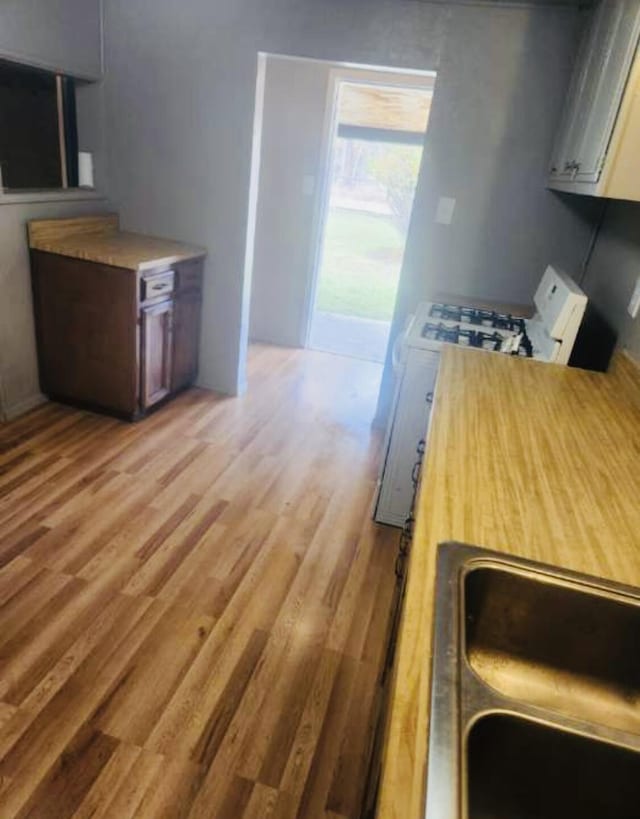 kitchen with a sink, light countertops, light wood finished floors, and white gas range