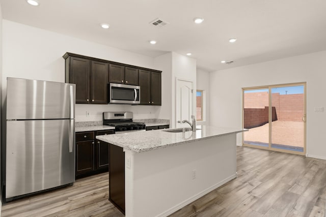 kitchen with a sink, light stone counters, light wood-style floors, and stainless steel appliances