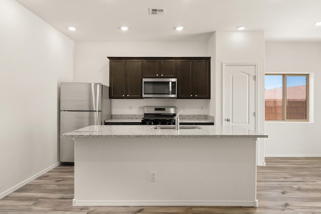 kitchen featuring a sink, light stone counters, stainless steel appliances, and light wood-style flooring