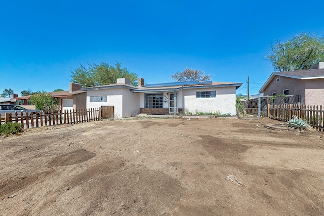 view of front of house with roof mounted solar panels, an attached garage, fence private yard, and stucco siding