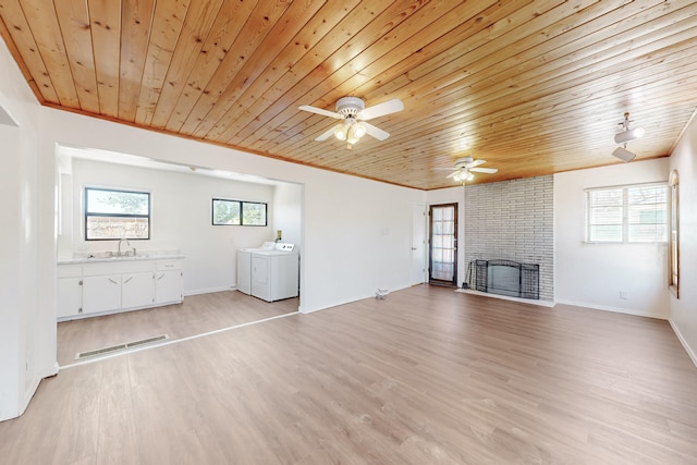 unfurnished living room featuring a ceiling fan, wooden ceiling, a sink, washing machine and clothes dryer, and a fireplace