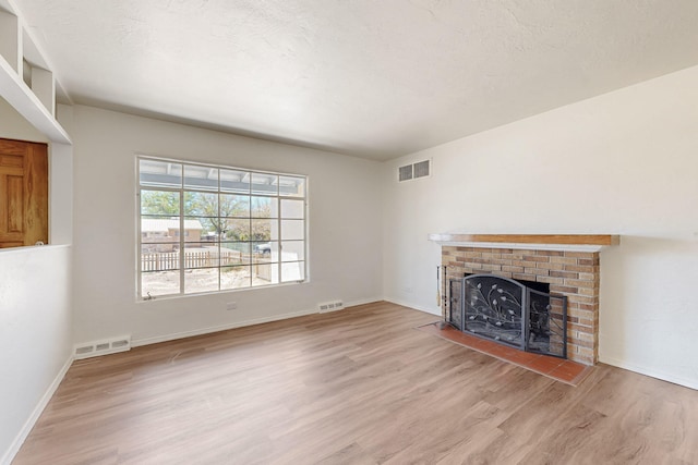 unfurnished living room with light wood-style floors, baseboards, visible vents, and a brick fireplace