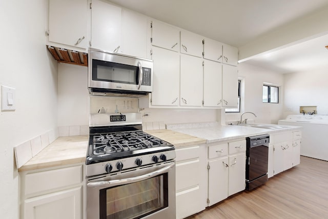 kitchen featuring a sink, white cabinets, light wood-type flooring, stainless steel appliances, and washing machine and dryer