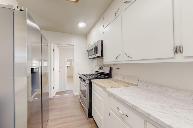 kitchen with white cabinets, light wood finished floors, baseboards, and stainless steel appliances