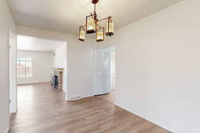 unfurnished dining area with a fireplace with flush hearth, baseboards, visible vents, and light wood-style floors