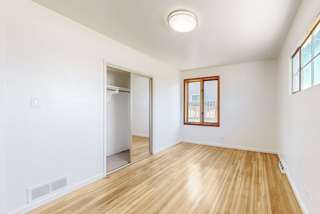 unfurnished bedroom with baseboards, visible vents, light wood-style floors, and a closet