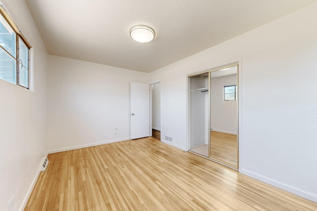 unfurnished bedroom featuring baseboards, light wood finished floors, visible vents, and a closet