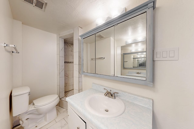 bathroom with vanity, marble finish floor, a tile shower, toilet, and visible vents