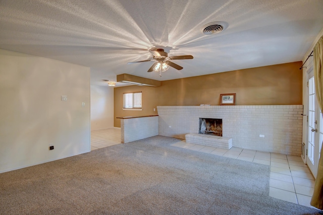 unfurnished living room featuring light tile patterned floors, a brick fireplace, a ceiling fan, visible vents, and light colored carpet