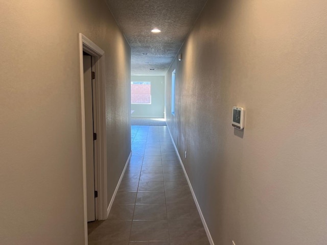 hall featuring tile patterned floors, baseboards, a textured ceiling, and a textured wall