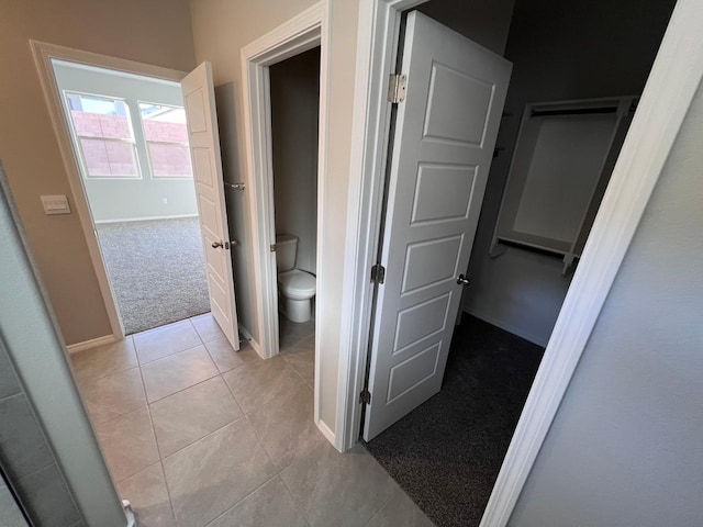 hall featuring baseboards, light tile patterned floors, and light colored carpet