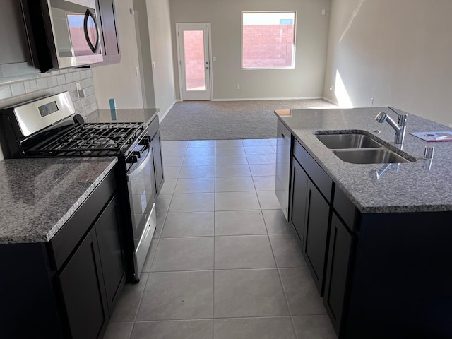 kitchen with light stone countertops, dark cabinets, stainless steel appliances, a sink, and open floor plan
