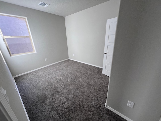 unfurnished room featuring visible vents, dark carpet, and baseboards