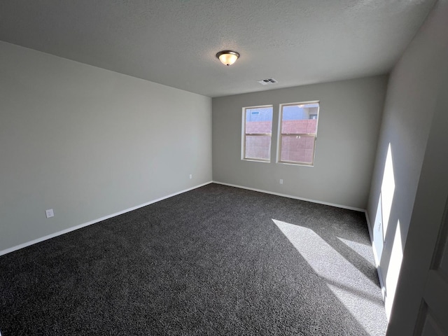 spare room featuring a textured ceiling, visible vents, dark carpet, and baseboards