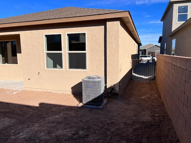 view of property exterior featuring fence, stucco siding, cooling unit, and roof with shingles