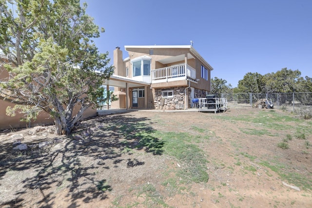 back of house featuring fence, a chimney, a balcony, and stone siding