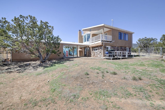 back of property with a chimney, fence, a balcony, and stone siding