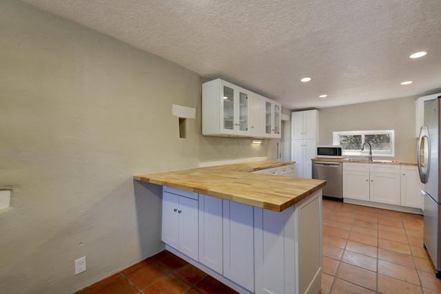 kitchen with recessed lighting, glass insert cabinets, a peninsula, wooden counters, and appliances with stainless steel finishes