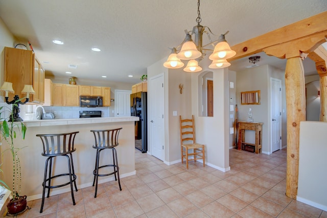 kitchen with an inviting chandelier, light brown cabinets, light countertops, black appliances, and a peninsula