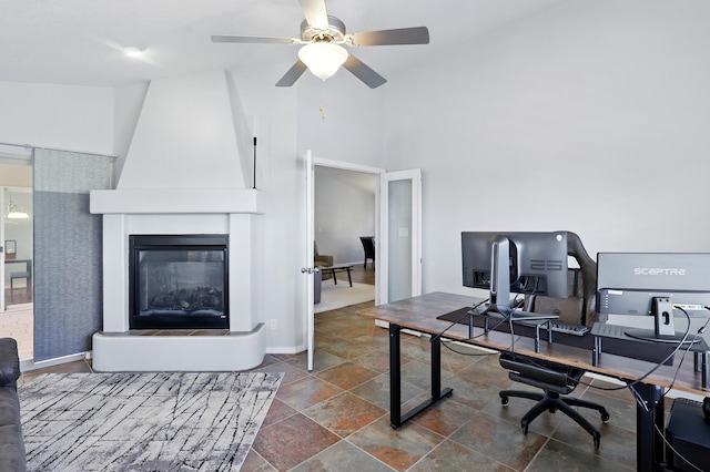 office area with stone finish floor, a large fireplace, baseboards, a ceiling fan, and high vaulted ceiling
