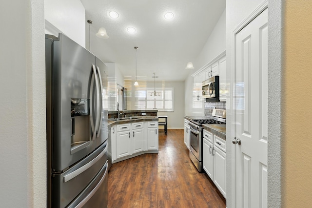 kitchen with stainless steel appliances, white cabinets, dark wood-style flooring, a sink, and a peninsula