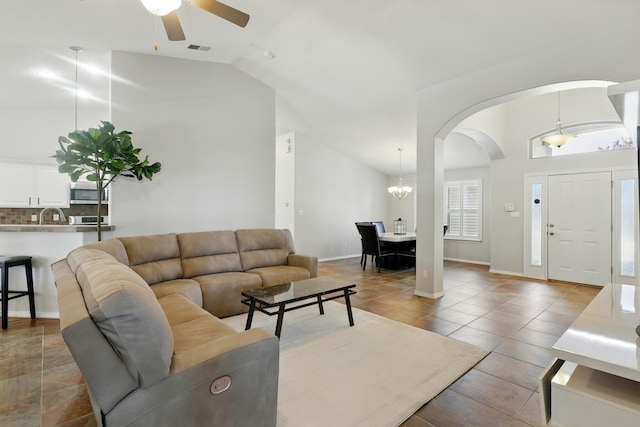 tiled living room with arched walkways, ceiling fan with notable chandelier, baseboards, visible vents, and lofted ceiling
