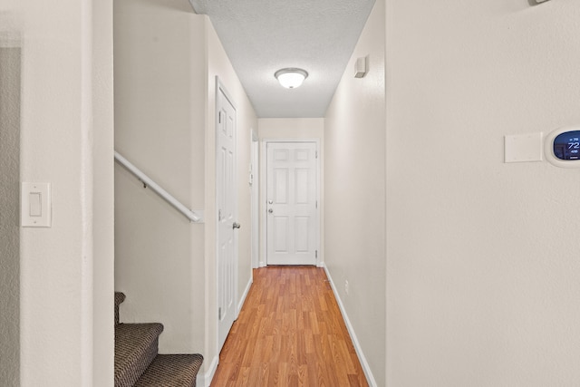 hall with baseboards, light wood-type flooring, and a textured ceiling