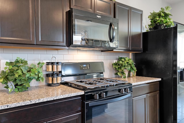 kitchen with dark brown cabinets, light stone countertops, decorative backsplash, and black appliances