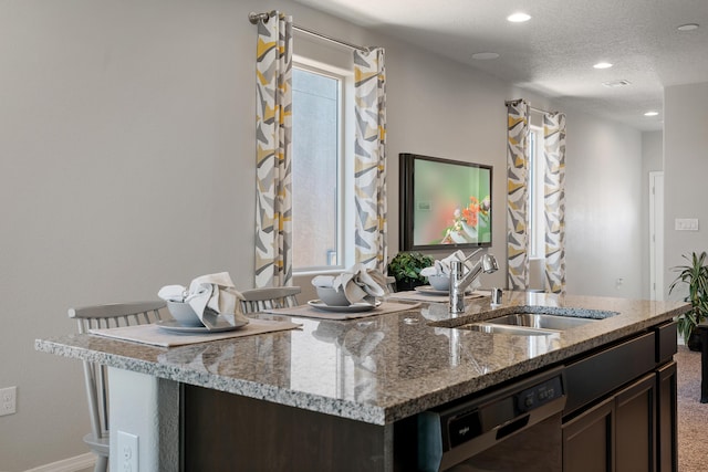 kitchen with recessed lighting, light stone counters, a sink, dark brown cabinetry, and black dishwasher