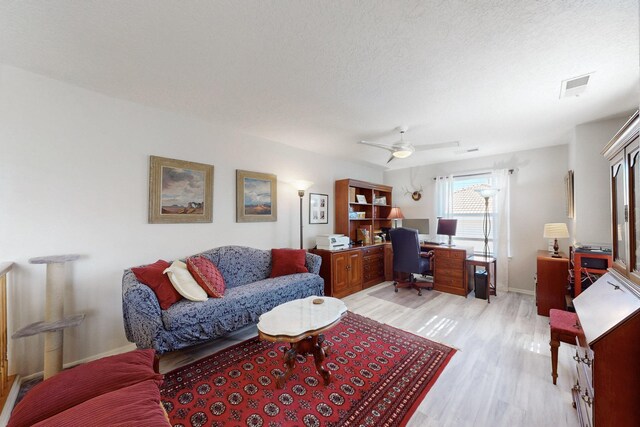 living area featuring a ceiling fan, visible vents, light wood-style flooring, baseboards, and a textured ceiling