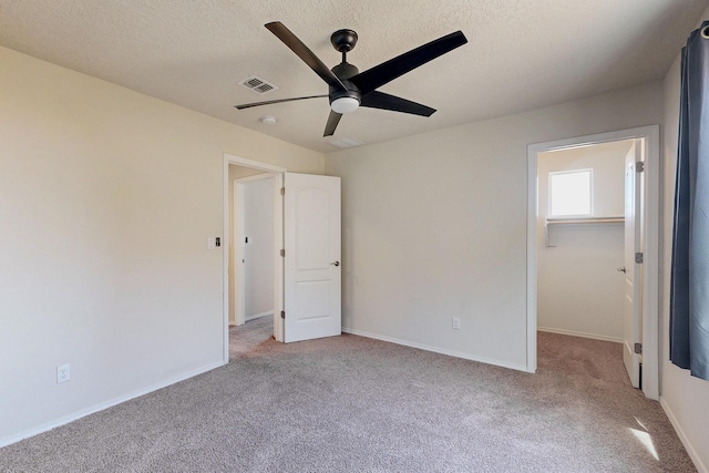 unfurnished bedroom with light colored carpet, visible vents, a textured ceiling, and a walk in closet