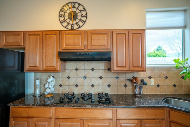 kitchen with dark stone counters, black appliances, backsplash, and under cabinet range hood
