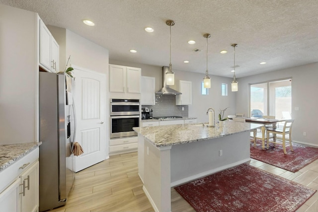 kitchen featuring light wood-style floors, appliances with stainless steel finishes, wall chimney range hood, and a sink