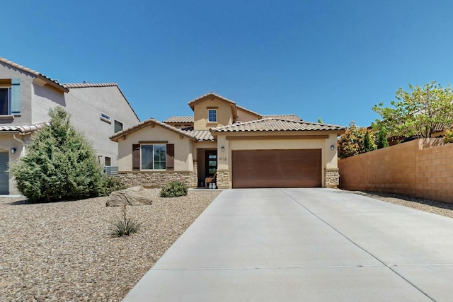 mediterranean / spanish house with fence, concrete driveway, stone siding, stucco siding, and a garage
