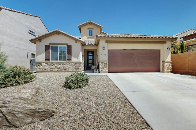 mediterranean / spanish-style home with stucco siding, a garage, a tile roof, stone siding, and concrete driveway