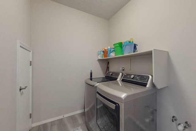 clothes washing area featuring laundry area, independent washer and dryer, light wood-style floors, baseboards, and a textured ceiling