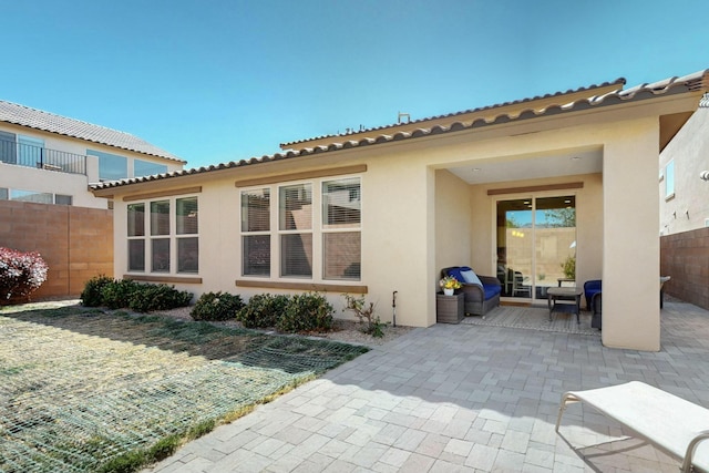 back of property with fence, stucco siding, a tile roof, and a patio area