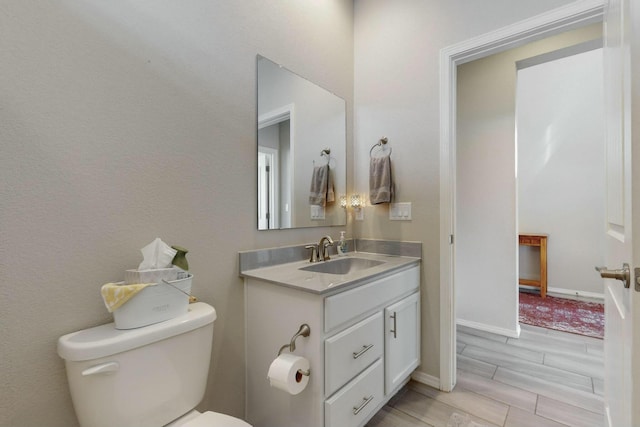 half bathroom featuring toilet, wood finish floors, vanity, and baseboards