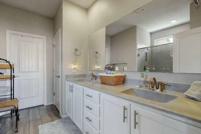 bathroom with double vanity, a sink, a shower stall, and wood finished floors