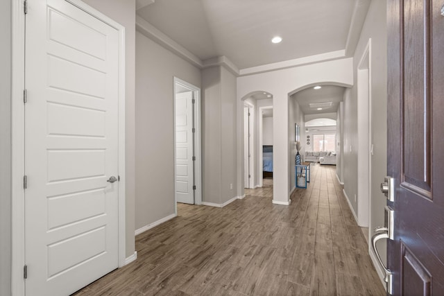 hallway with wood finished floors, baseboards, recessed lighting, and arched walkways