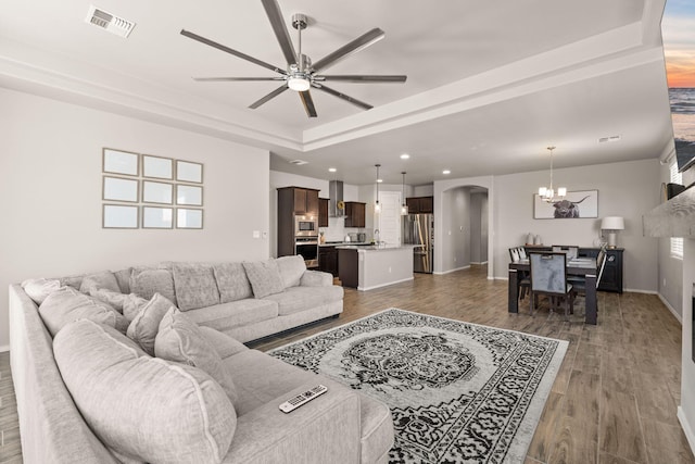 living area with recessed lighting, arched walkways, wood finished floors, ceiling fan with notable chandelier, and a tray ceiling