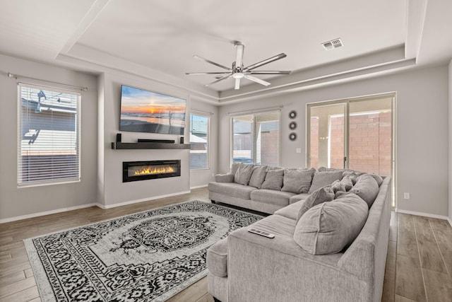 living area featuring wood finished floors, a raised ceiling, a ceiling fan, and visible vents