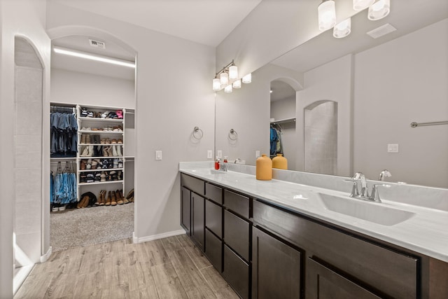 full bathroom with a sink, double vanity, visible vents, wood finished floors, and a walk in closet