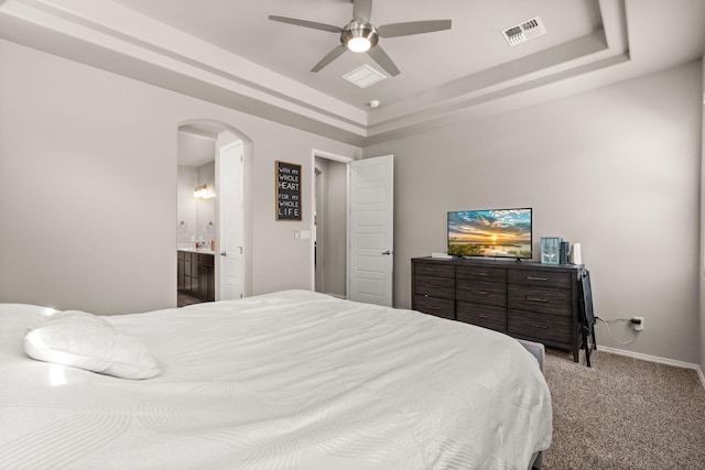 bedroom featuring carpet, visible vents, a tray ceiling, and arched walkways
