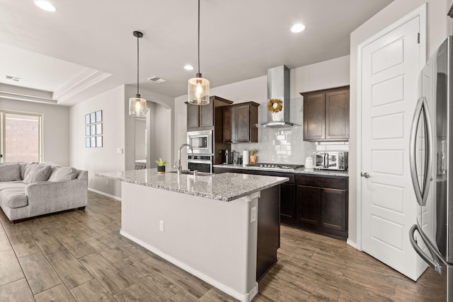 kitchen with appliances with stainless steel finishes, dark brown cabinetry, baseboards, arched walkways, and wall chimney exhaust hood