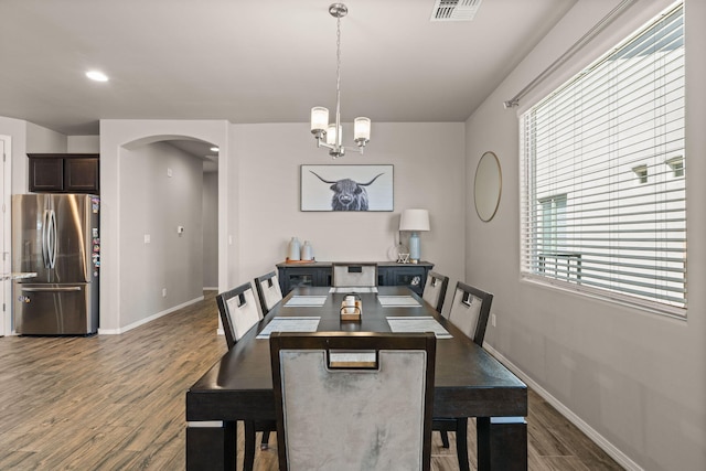 dining space with arched walkways, a healthy amount of sunlight, wood finished floors, visible vents, and a notable chandelier