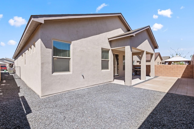 rear view of property featuring stucco siding, fence, and a patio