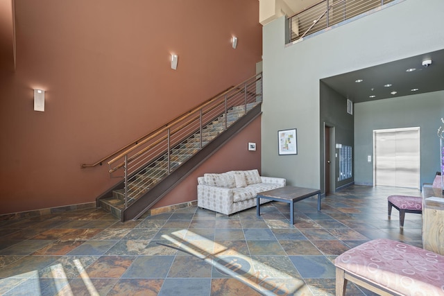 living room with stone tile floors, baseboards, stairs, and a high ceiling